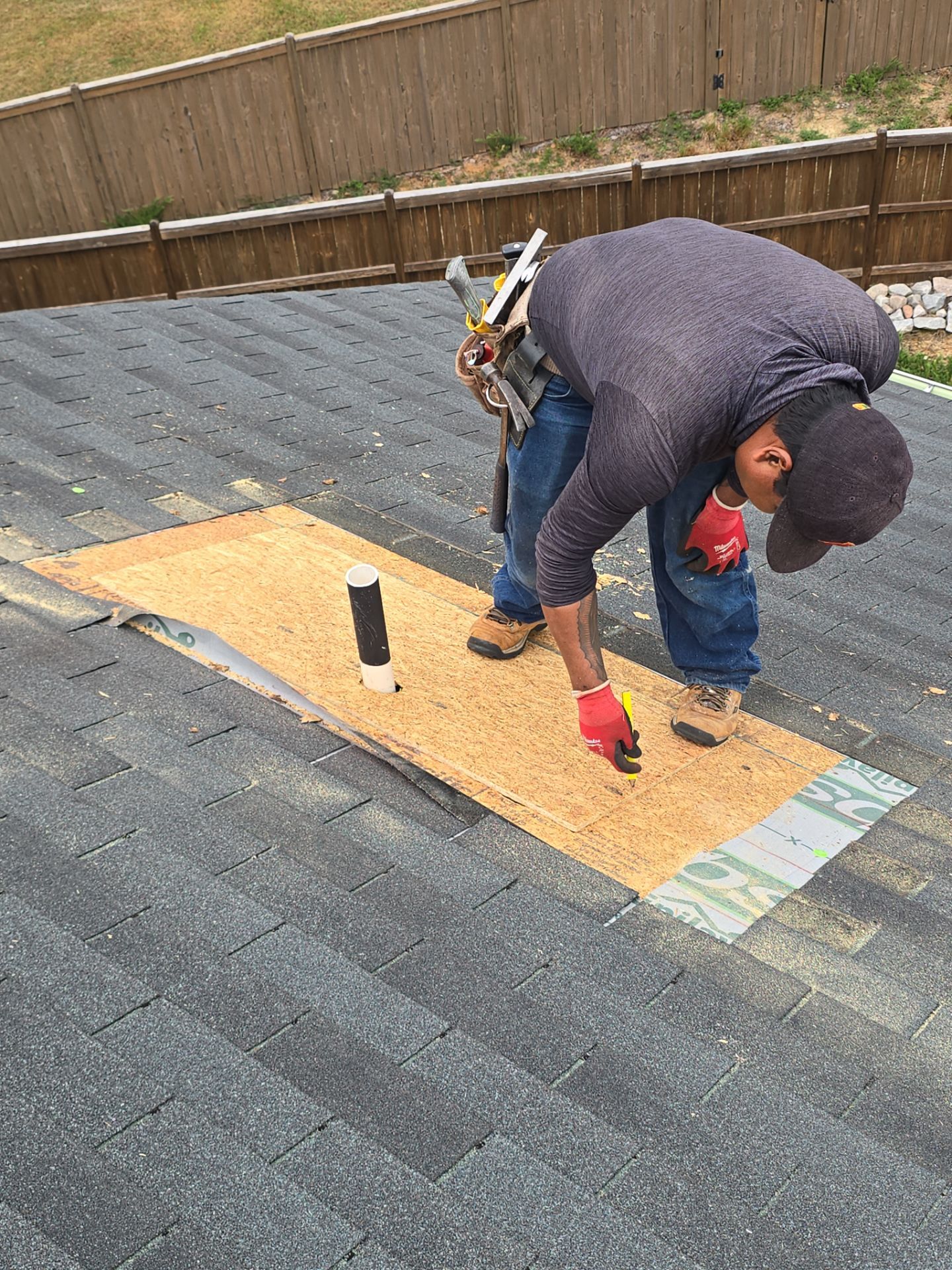 Worker nailing plywood patch over roof hole emergency repair Raleigh NC